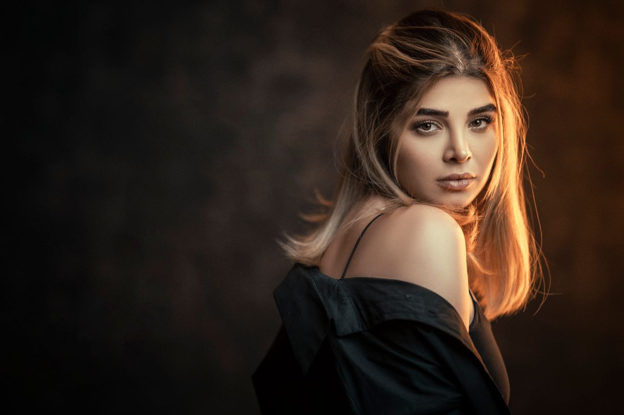 Glamorous woman posing in a studio with a dark background and elegant lighting.