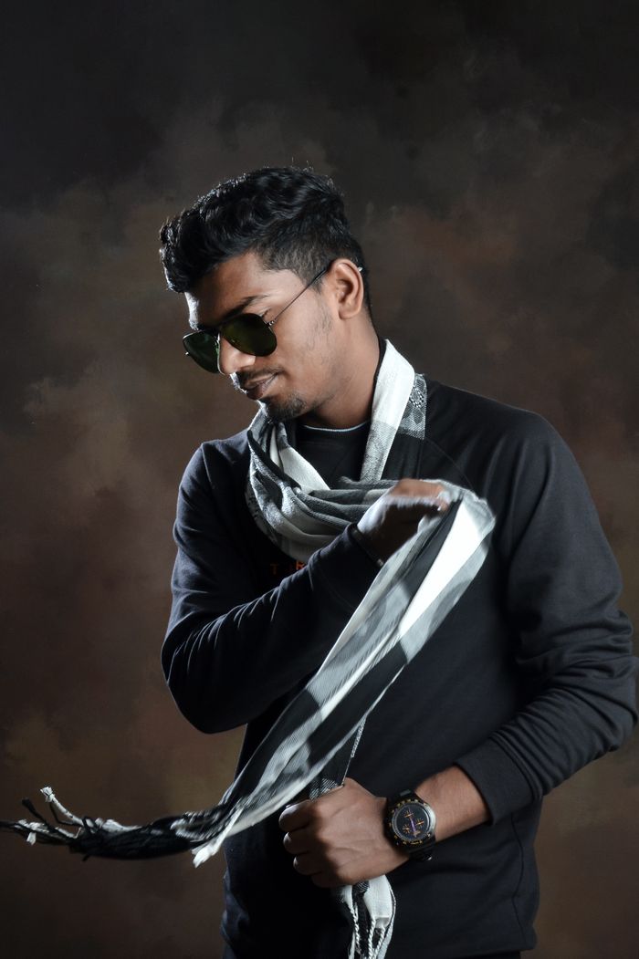 contact-img Portrait of a fashion-forward man in sunglasses and scarf against a dark background.