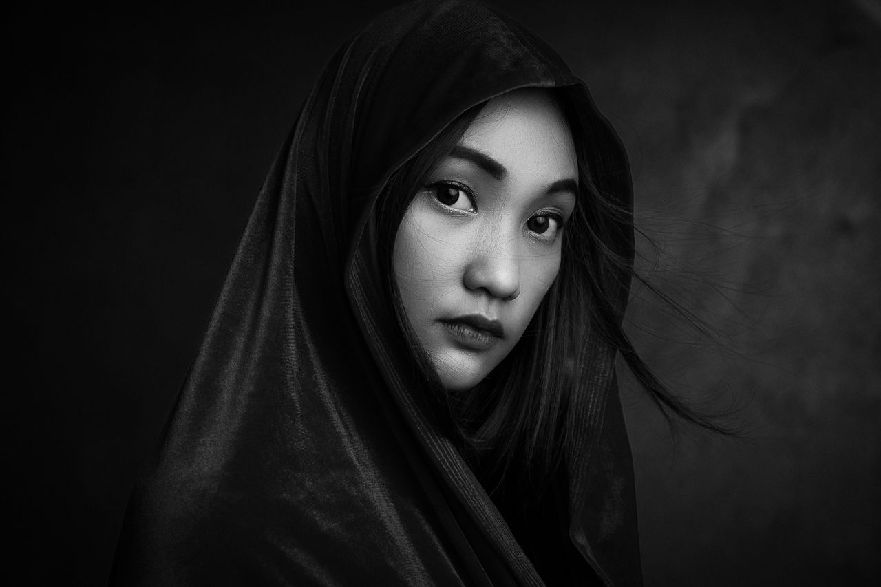 Elegant black and white portrait of a woman with a hooded cloak, exuding a moody and artistic tone.