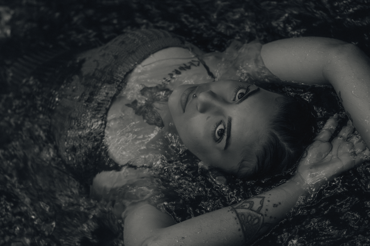 services-img Artistic black and white portrait of a woman with tattoos laying in water.